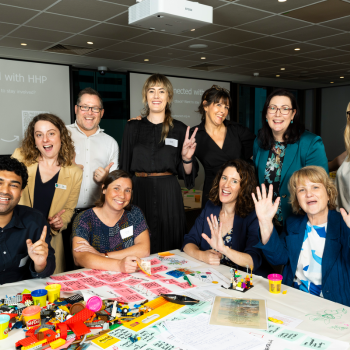 Group of nine people smiling and posing around a table scattered with craft materials during a workshop session.
